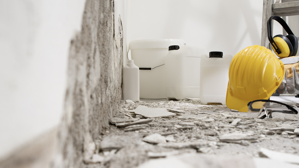 house renovation concept, wall in demolition with plaster rubble and protective construction work tools, paints, primer, buckets and jerry cans of building products, white background with copy space